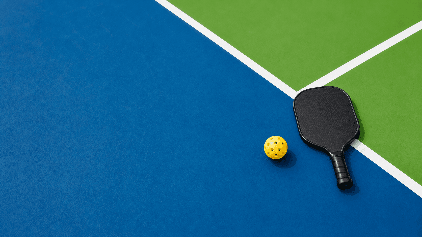 Pickleball court with a paddle and yellow ball